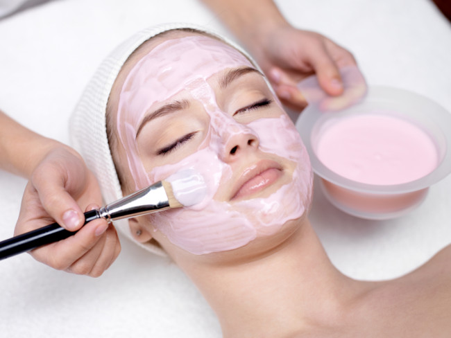 Ung vacker tjej som får rosa ansiktsmask i spa skönhetssalong - inomhus