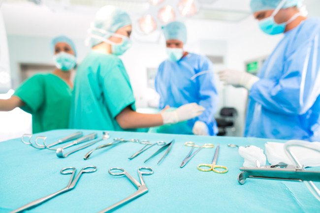 Nemocničný - chirurgický tím v operačnej miestnosti alebo OP kliniky pôsobiaceho na pacienta, snáď's an emergency a assistant holding a cotton swap forceps