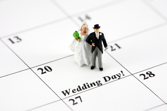 Imaginea conceptuală a unei mirese și mirele în picioare pe o dată calendaristică care spune ziua nunții.