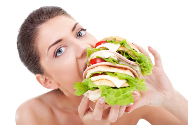 زن جوان خوردن یک ساندویچ بزرگ در پس زمینه سفید