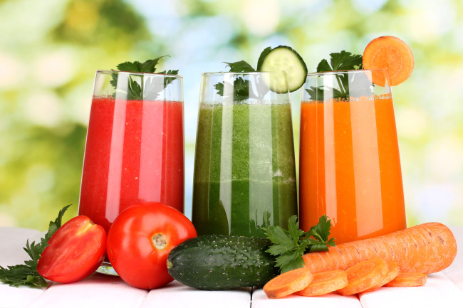 Fresh vegetable juices on wooden table, on green background