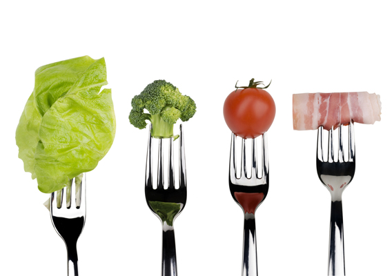 Broccoli, tomato, lettuce salad and slice of bacon on forks isolated on a white background.