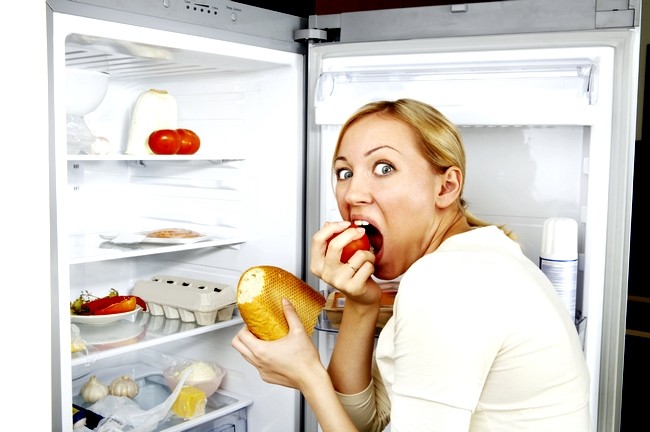 The woman greedy eats meal against an open refrigerator