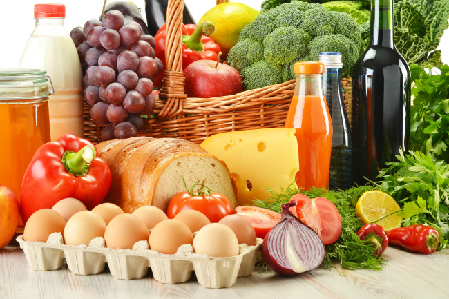 Groceries in wicker basket including vegetables, fruits, bakery and dairy products and wine isolated on white