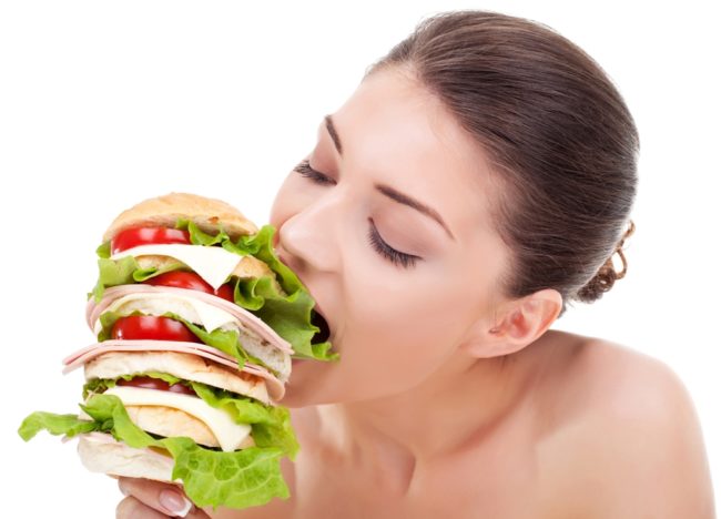 young woman biting a big sandwich, isolated on white background
